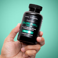 Hand holding Vital Vitamins Chlorophyll Complex bottle against teal background - superfood detox supplement